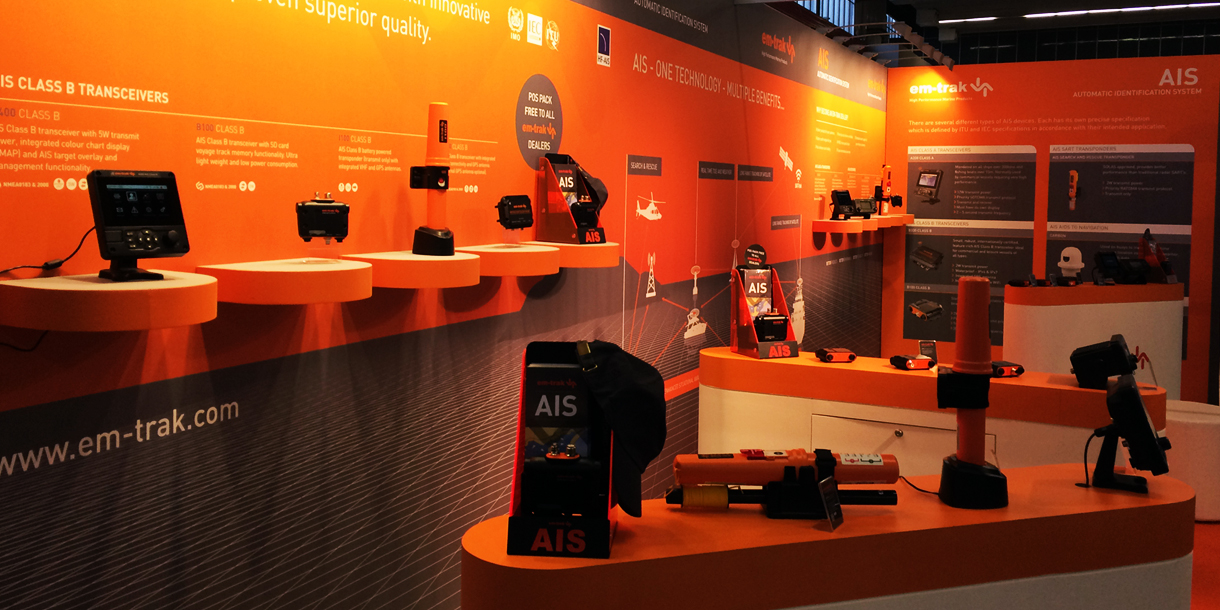 em-trak AIS Class B transceivers and marine electronics displayed on orange counter top displays at a trade exhibition stand
